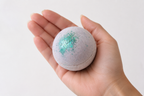 Boule de bain mangue tenue dans une main pour montrer la taille du produit.