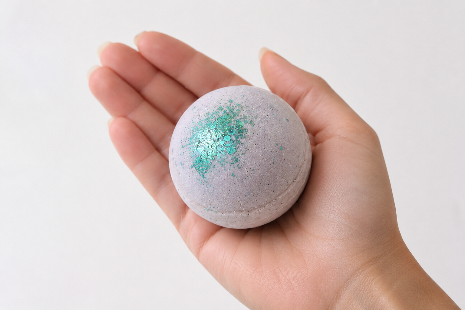 Boule de bain mangue tenue dans une main pour montrer la taille du produit.